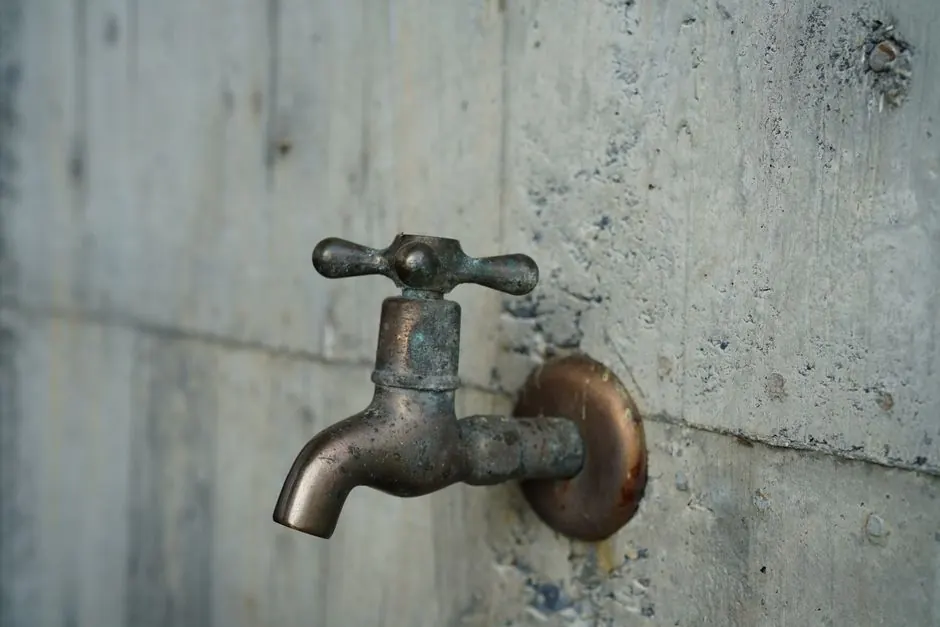 A detailed view of an aged metal faucet mounted on a textured concrete wall, revealing patina.